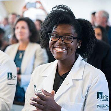 A smiling black, female medical student gets her white coat.