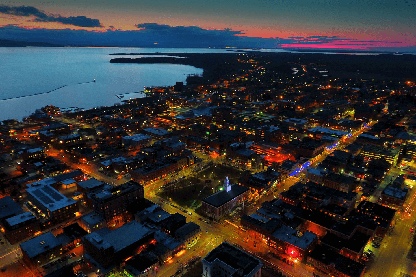 Aerial view of Burlington and the UVM Campus at sunset accented by colorful lights and the lake.