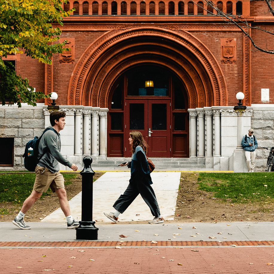 Students walk past an arched entryway to a classic campus building.