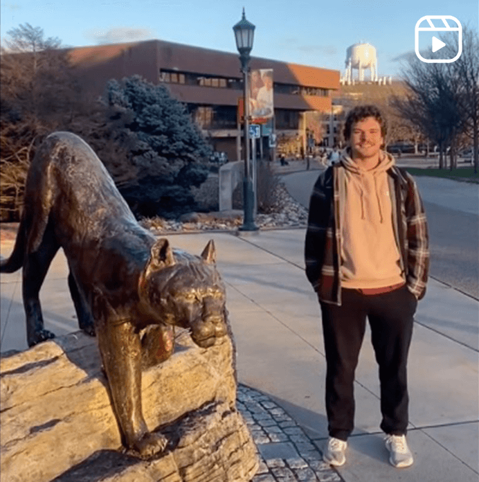 A student poses next to the iconic bronze catamount sculpture.